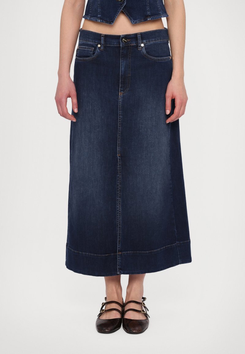 Mörkblå denimmaxikjol med rak skärning, fem fickor och sömnadsdetaljer. Matchad med mörka skor med remmar.