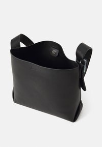 Must Black leather bag minimalist disainiga, sujuva tekstuuriga, avatud ülaservaga ja metallist nuppkinnitusega. Reguleeritav rihm kaasas.