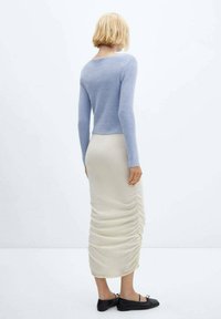 Lichtblauwe gebreide trui met lange mouwen en een ronde hals, gecombineerd met een crèmekleurige gerimpelde midi-rok en zwarte platte schoenen.