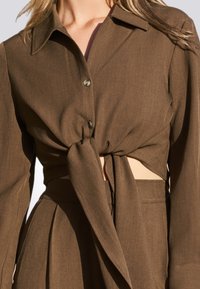 Bruine button-up shirt met lange mouwen, voorzien van een geknoopte voorkant en uitsnijdingen aan de zijkanten. Gemaakt van gestructureerde stof met een getailleerd ontwerp.