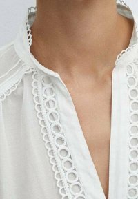 Witte blouse met een ronde kraag, delicate, ronde kantafwerking langs de halslijn en de knoopsluiting, en lichtgewicht, doorschijnende stof.