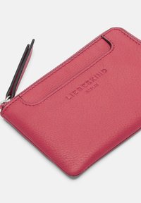 Porte-cartes en cuir rose avec une finition texturée, doté d'une fermeture éclair, d'un emplacement pour cartes et d'un marquage en relief sur le devant.