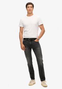 Camiseta blanca de algodón, jeans de mezclilla negros y zapatillas de color claro. Presenta un corte clásico, con una textura suave y un diseño minimalista.