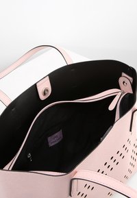 Roze synthetische handtas met een perforatiedesign, zwarte binnenkant, twee handvatten en een ritsvak aan de binnenkant. Heeft een logo-label.