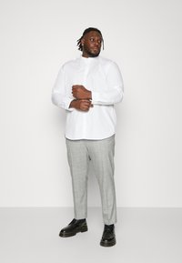 Weißes Langarm-Hemd mit Knöpfen, kombiniert mit hellgrauen karierten Hosen. Schwarze Schnürschuhe runden das Outfit ab. Einfaches und formelles Design.