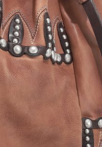 Bruin leren materiaal met ingewikkelde accenten van zilverkleurige hardware en gevlochten stiksels. Gelaagde oppervlakte met opvallende klinknagels en decoratieve randen.