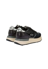 Zwarte sneakers met een gestructureerde zwarte en zilveren hiel, een contrasterende beige tussenzool en een glanzend zilveren logo op de achterkant.