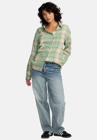 Camicia a quadri verdi con bottoni in tessuto leggero, abbinata a jeans blu larghi e scarpe nere con strisce bianche. Look casual e stile rilassato.
