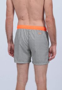 Shorts de bain avec un motif géométrique noir et blanc, dotés d'une taille élastique orange, d'une longueur mi-cuisse, d'une coupe décontractée et d'une texture lisse.