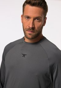 Graues langärmeliges Sportshirt mit Rundhalsausschnitt und Raglanärmeln. Verfügt über ein dezentes schwarzes Logo auf der Brust und eine glatte Textur.