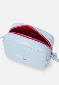 Borsa a tracolla rettangolare di colore azzurro chiaro, realizzata in pelle, con una fodera interna rossa, zip argentate e logo stampato sul frontale.