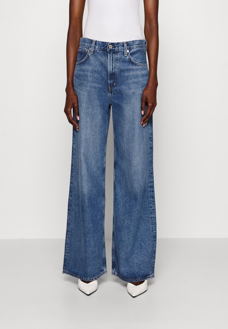 Bredde ben denimjeans i lys blå vask, med høyt liv, klassisk femlommers design og rå kant. Brukt med hvite spisse sko.