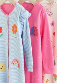 Drie baby rompers: blauw gestreept met een bloem en een regenboog, roze met een lieveheersbeestje, en lichtroze met kleurrijke patronen. Zacht katoenen stof, ronde hals.