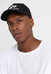 Svart mesh caps med en hvit logo, sammen med en enkel hvit t-skjorte med crew neck. Capsen har en strukturert form og buet skjerm.