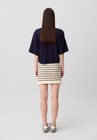 Top court bleu marine à manches courtes, associé à une mini-jupe crème à rayures avec un ourlet volanté. Chaussures bleu clair avec des accents blancs.