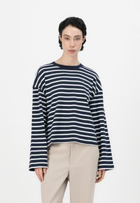 Una blusa de rayas en azul marino y blanco de manga larga con cuello redondo y mangas anchas, hecha de tela suave, combinada con pantalones beiges.