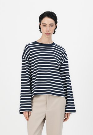 Marineblå og hvite stripete langermet topp med rund hals og vide ermer, laget av mykt stoff, sammen med beige bukser.