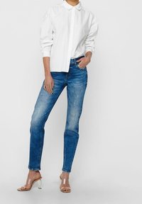 Vit skjorta med puffärmar, kombinerad med ljusblå jeans och genomskinliga klacksandaler, med en klassisk rak skärning och lätt slitningar.