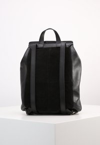 Černý kožený batoh se suede panely, vybavený dvojitými ramenními popruhy a horní rukojetí. Hladký povrch s prošívanými detaily.