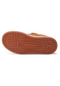 Semelle de sneaker marron avec des motifs de grille et de zigzag, comportant le texte "DCSHOECOUSA" et le logo étoile de DC Shoes près du talon.