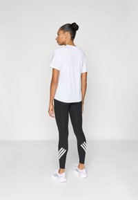 Weißes Sport-T-Shirt, schwarze Leggings mit drei weißen Streifen an den Seiten und weiße Turnschuhe mit einem hellrosa Akzent an der Ferse.