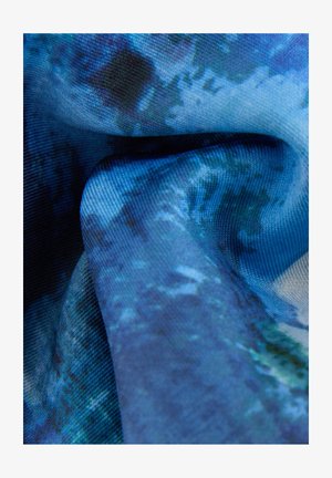 Modra tkanina z gladko teksturo, ki prikazuje abstraktne vzorce v različni modri, zeleni in črni barvi, poudarjajoč tekstilni dizajn.