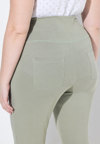 Zelené legíny s vysokým pasem vyrobené z elastické tkaniny. Obsahují dvě zadní kapsy a bezešvý design s jemným žebrováním a lehkým šitím.