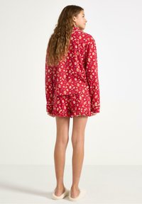 Rode pyjama set met lange mouwen top en shorts, met gouden gemberbrood en feestelijke patronen. Zachte stof met een gerimpelde zoom op de shorts.