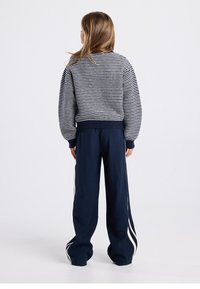 Navy striped sweater with ribbed cuffs, paired with loose navy pants featuring white side stripes. Soft knit texture and relaxed fit.