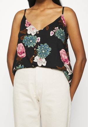 Débardeur noir à fleurs avec des fleurs roses et bleues, décolleté en V, bretelles fines et détails de boutons à l'avant, associé à un pantalon de couleur claire.