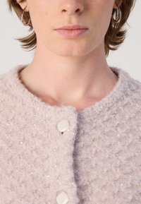 Lichtroze cardigan met een gestructureerd breipatroon en kleine pailletjes. Het heeft een ronde halslijn en twee crèmekleurige knopen.
