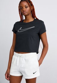 Fekete, rövidített póló fehér Nike logóval, fehér izzadság rövidnadrággal párosítva, amelyen egy kis fekete logó található. Pamut anyag, laza illeszkedés.