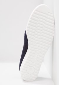 Navy semišová bota s bílou gumovou podrážkou, která má texturovaný vzor, navržená pro pohodlí a stabilitu. Obsahuje minimální detaily značky.