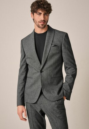 Grau karierter Blazer mit Reverskragen, Ein-Knopf-Verschluss und zwei vorderen Taschen. Kombiniert mit einem schwarzen Rundhals-Shirt.