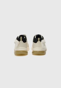 Beige sportieve schoenen met een gestructureerd oppervlak, zwarte accenten, rubberen zolen en een subtiele vachtdetail op de hiel.