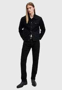 Chaqueta de mezclilla negra con botones al frente, dos bolsillos en el pecho y un corte entallado, combinada con jeans negros y elegantes botas negras.