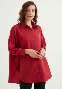 Rotes Button-Up-Hemd mit entspannter Passform, langen Ärmeln und abgerundetem Saum. Hergestellt aus glattem Material, mit klassischem Kragen und vorderen Knöpfen.