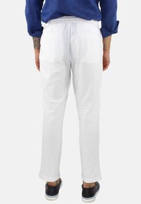 Pantaloni bianchi di lino con una vestibilità rilassata, dotati di una vita e due tasche posteriori. Abbinati a sneaker nere.