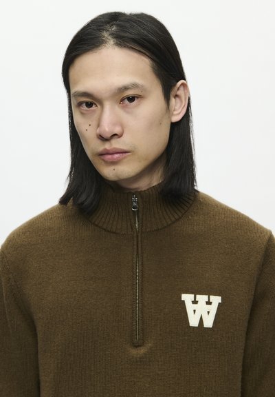 Gilet zippé marron avec col côtelé et un petit logo 'W' brodé en blanc sur le côté gauche. Texture douce, design ajusté.