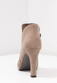 Beżowe zamszowe botki sięgające kostki z wąskim noskiem i wysokim obcasem w stylu stiletto. Charakteryzują się gładką teksturą i subtelnym przeszyciem z tyłu.