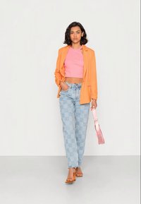 Orange blazer over en pink crop top, parret med lyseblå ternede jeans og brune hælede sandaler. Holder en pink håndtaske.