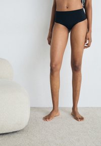 Bikini bottom neri a vita alta realizzati in un tessuto liscio ed elastico, caratterizzati da un design senza cuciture e un taglio minimalista.