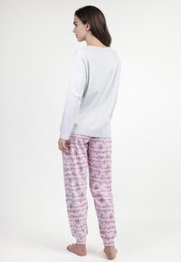 Blusa gris de manga larga combinada con pantalones de pijama rosa que presentan patrones caprichosos y puños elásticos. El material parece suave y cómodo.