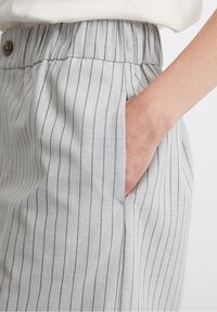 Pantalones grises a rayas con cintura elástica, bolsillos laterales y una textura de tela suave. Detalle incluye un botón en la cintura.