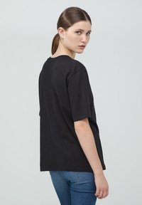 T-shirt in cotone nero con vestibilità rilassata e maniche corte, dotata di scollatura rotonda e design semplice senza elementi grafici.