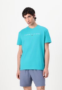 Turquoise katoenen T-shirt met een ronde hals en korte mouwen, met het "TOMMYJEANS"-logo in het wit gedrukt en een kleine vlagdetail.