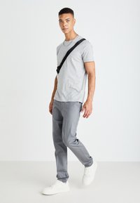 Grå t-skjorte med korte ermer kombinert med lysegrå bukser, komplementert av hvite joggesko. Syklingremmen gir funksjonell detalj. Minimalistisk design.