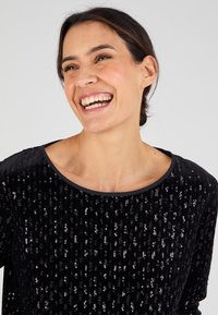 Top negro con lentejuelas, de escote redondo, con una textura suave y acentos brillantes, que destacan el patrón de lentejuelas superpuestas.
