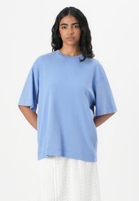Lys blå oversized t-skjorte laget av mykt stoff, med rund hals, korte ermer og en avslappet passform. Glatt tekstur med minimal detaljer.