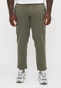 Pantalones tailored en verde oliva, con una textura suave y corte recto, combinados con zapatillas gris y blanco.